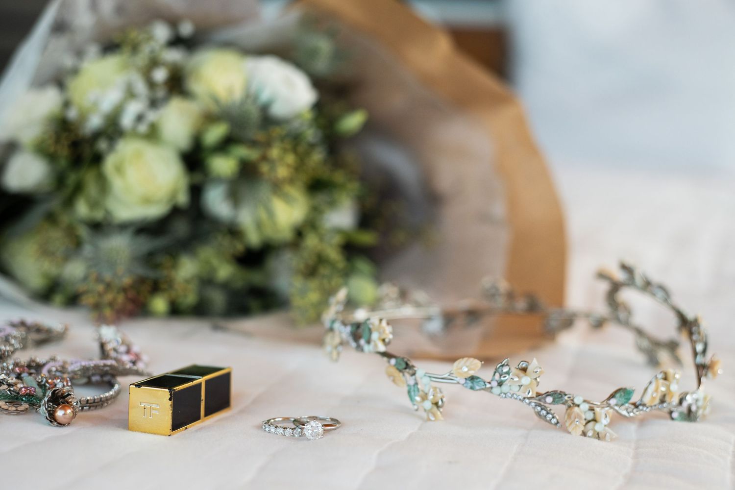 Wedding accessories including a floral crown, rings, and bouquet arranged on a light surface.