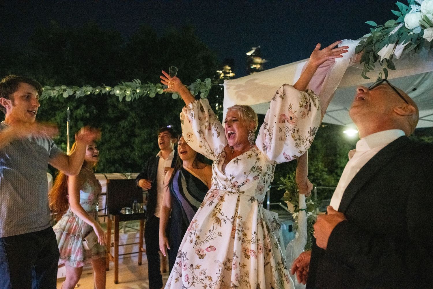 Wedding celebration with guests dancing and cheering under string lights at night.