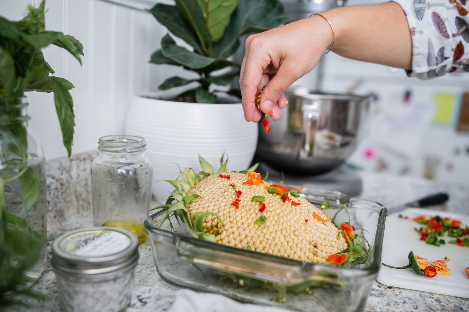 Someone garnishes a baked dish with fresh herbs in a bright kitchen setting.