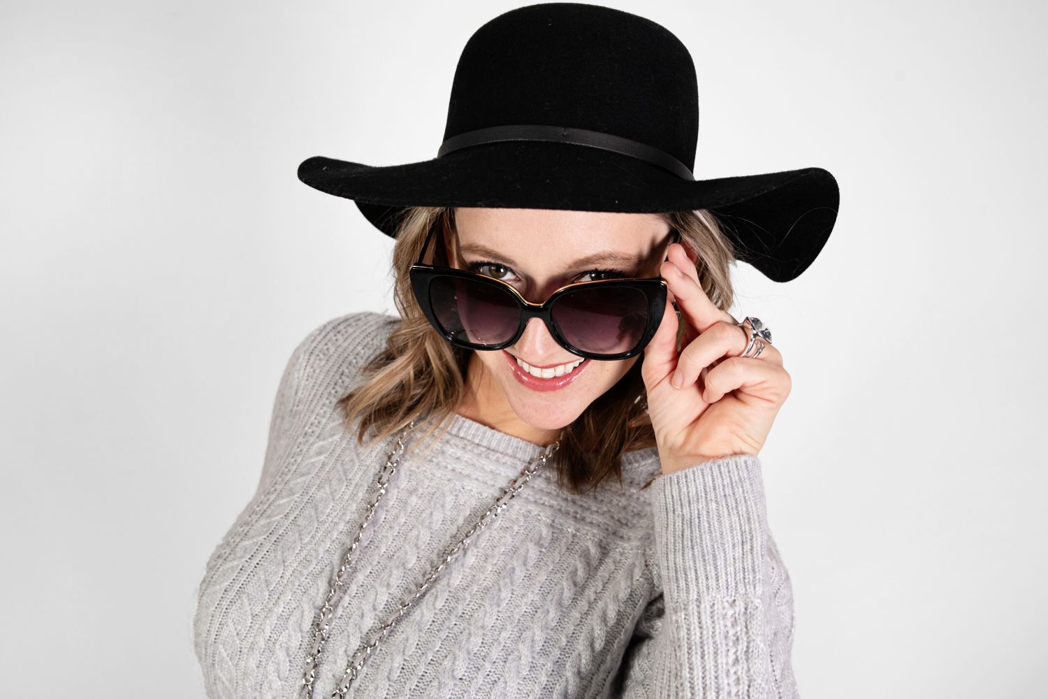 Winter style featuring grey sweater, black floppy hat and sunglasses against white background.