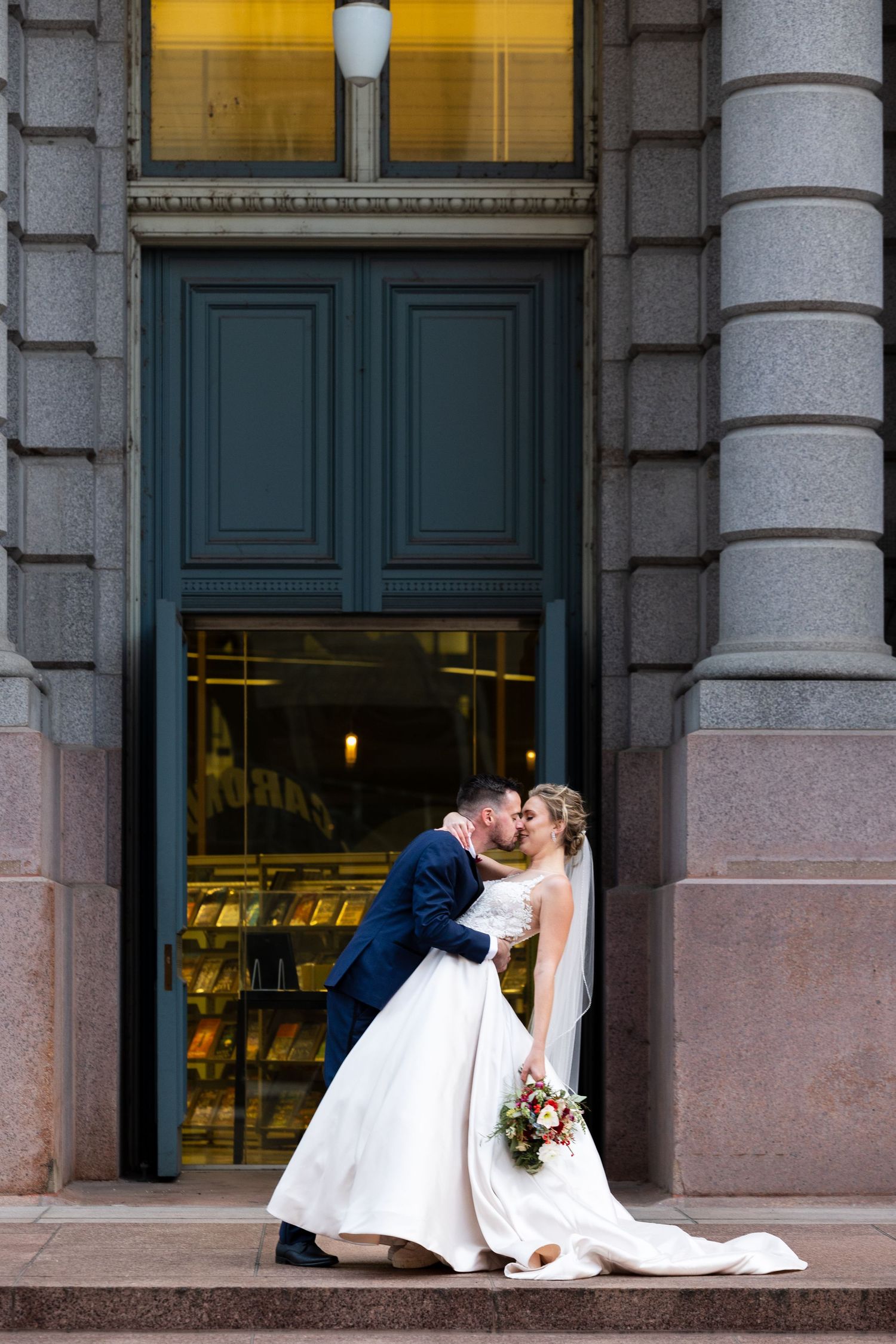 Romantic wedding kiss on grand stone steps with blue doors and warm lighting.