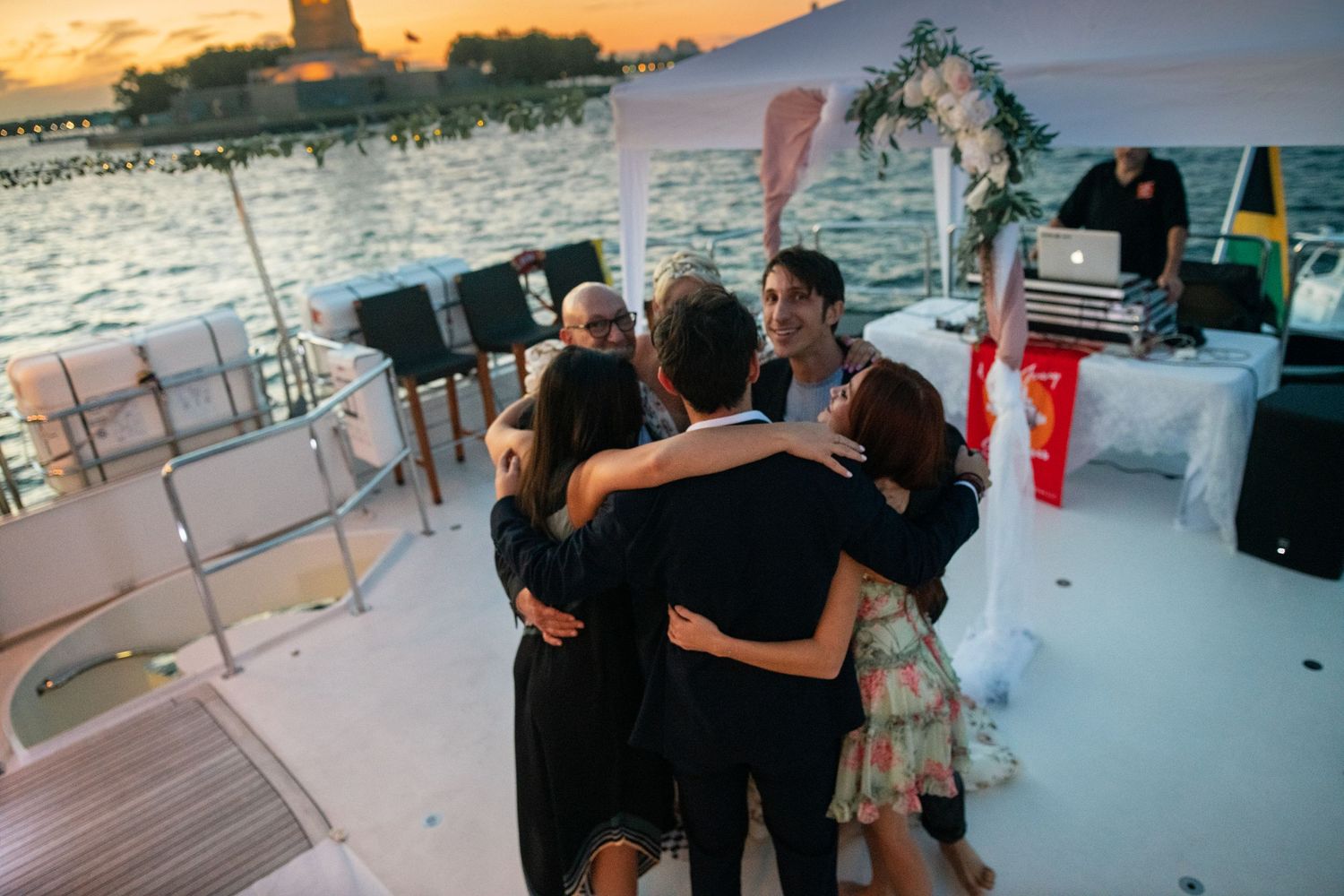 A group embraces in a warm hug during a celebration on a boat deck at sunset.