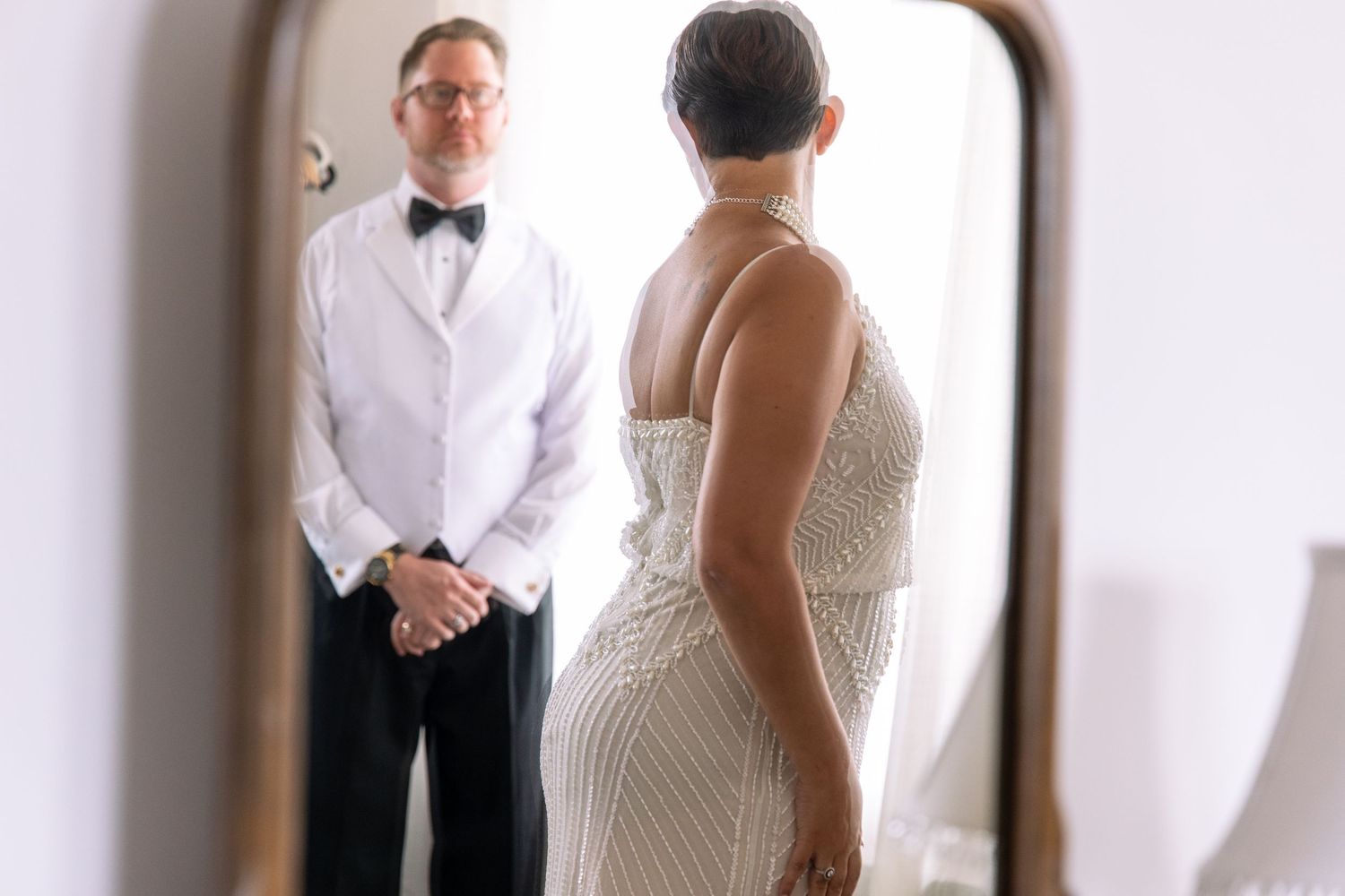 A reflection in an ornate mirror shows a couple in formal white attire.