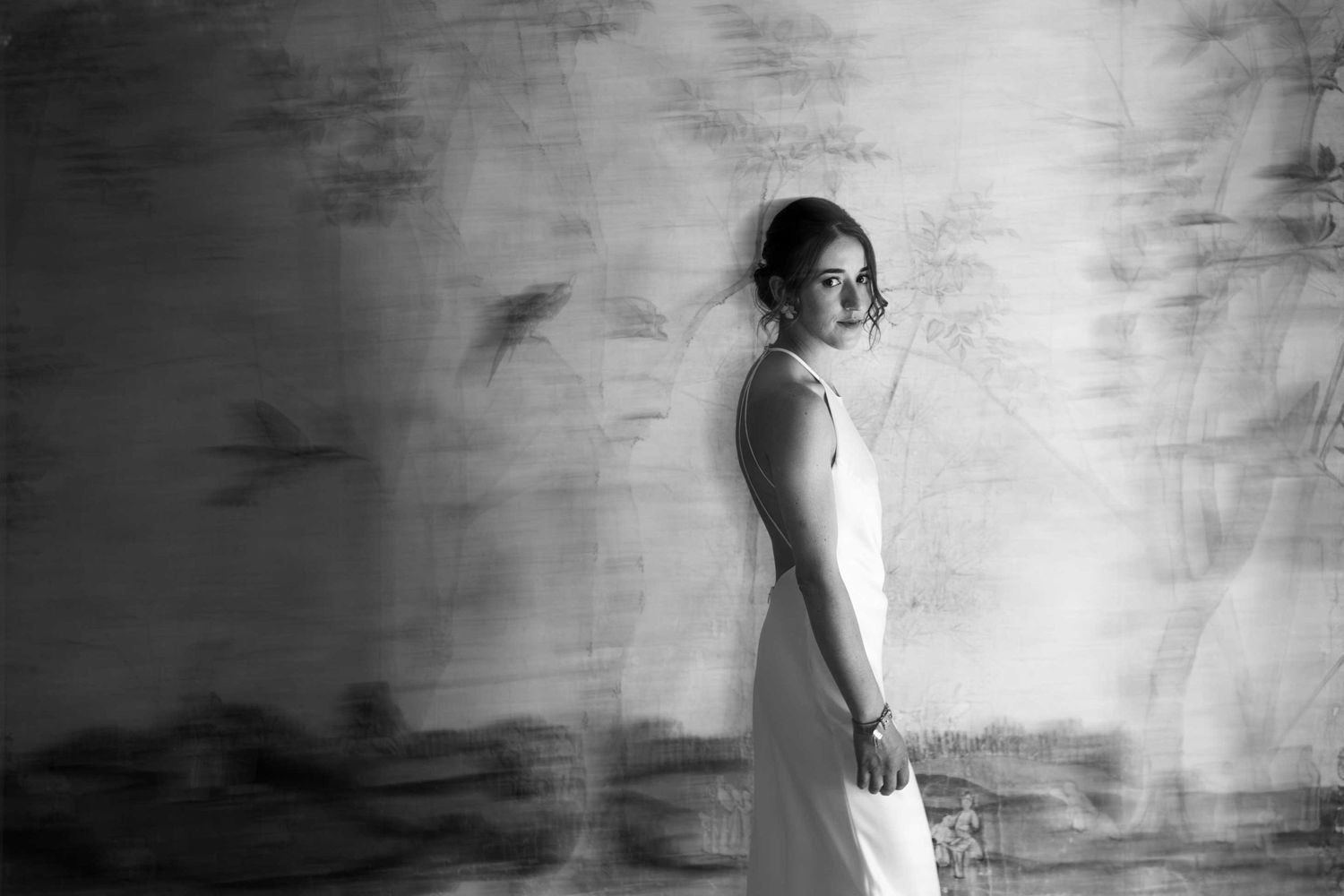 Artistic black and white portrait of a person in a wedding dress against a textured wall.