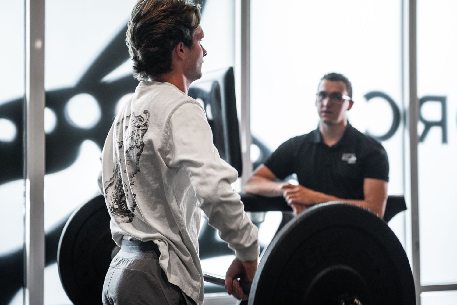 A training session in a gym with weight lifting equipment and large windows.