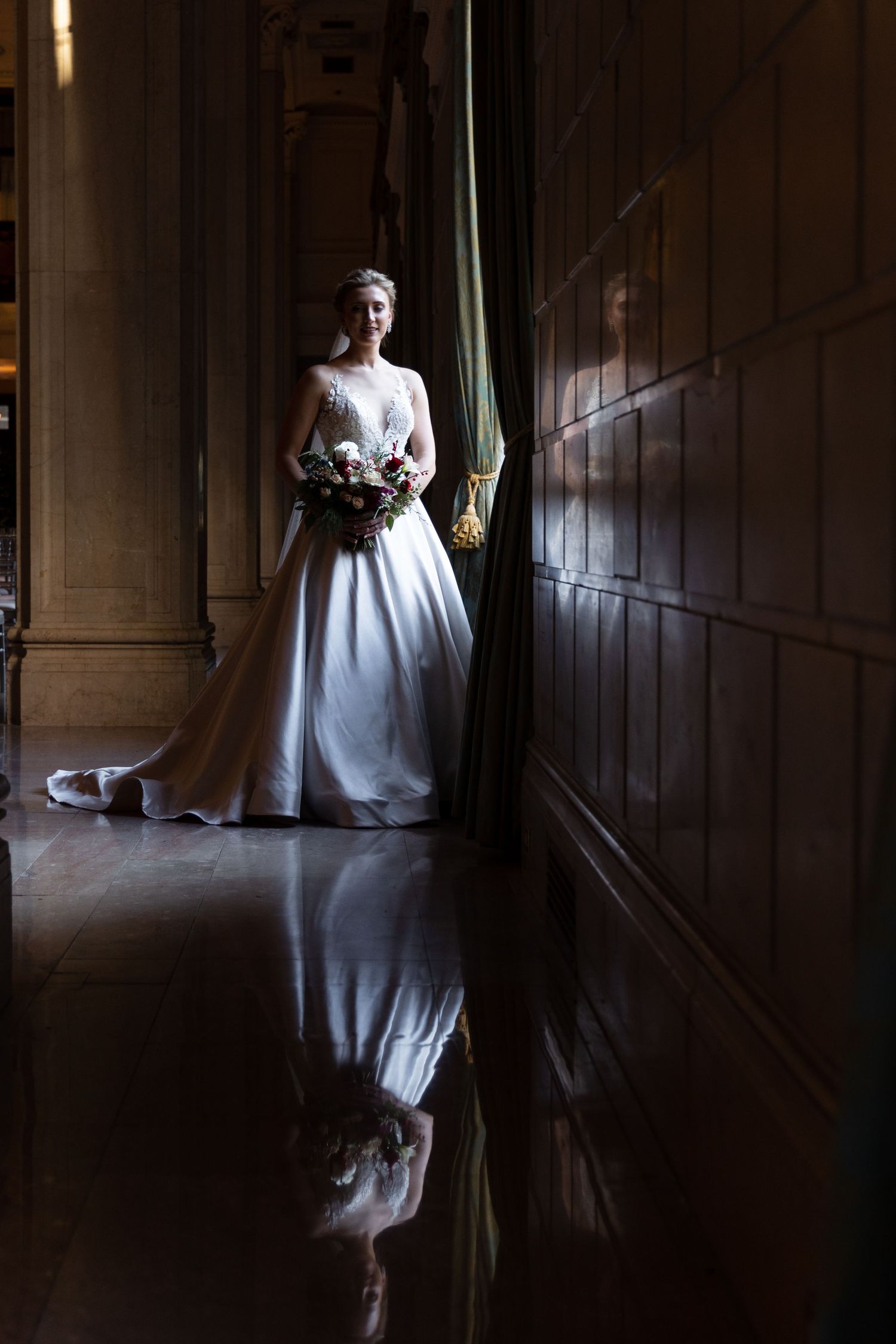 Dramatic bridal portrait in dark hallway with floor reflection and natural window light.