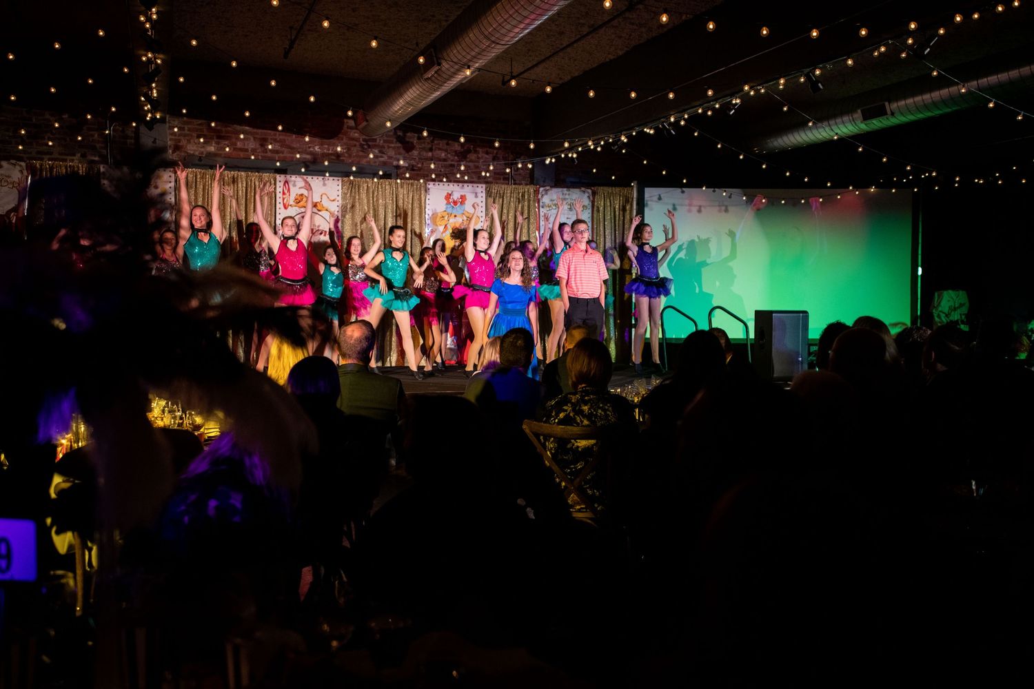 Dancers perform on illuminated stage with string lights and dramatic colored lighting effects.