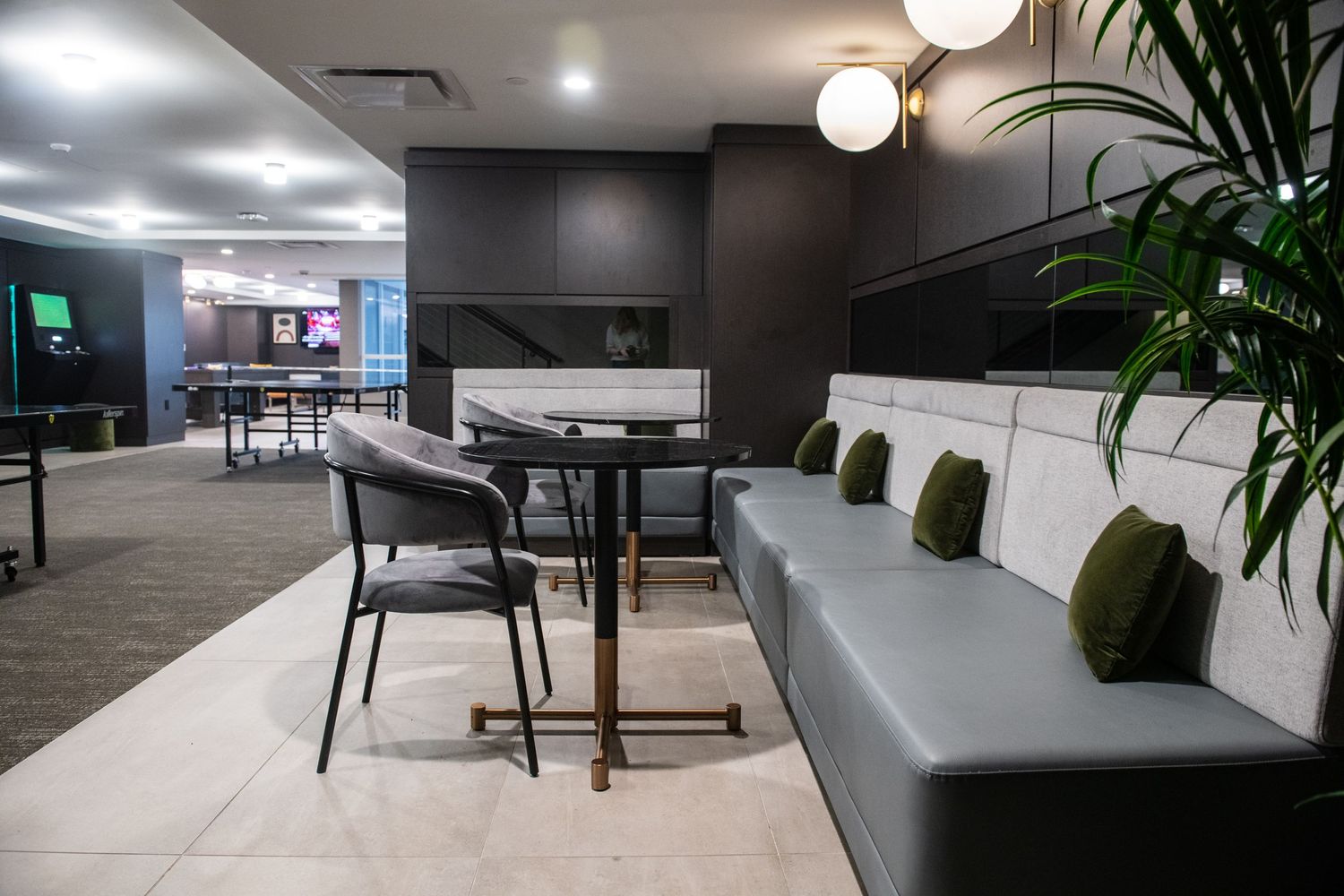 Modern office lounge area with grey seating, tables and decorative plants.