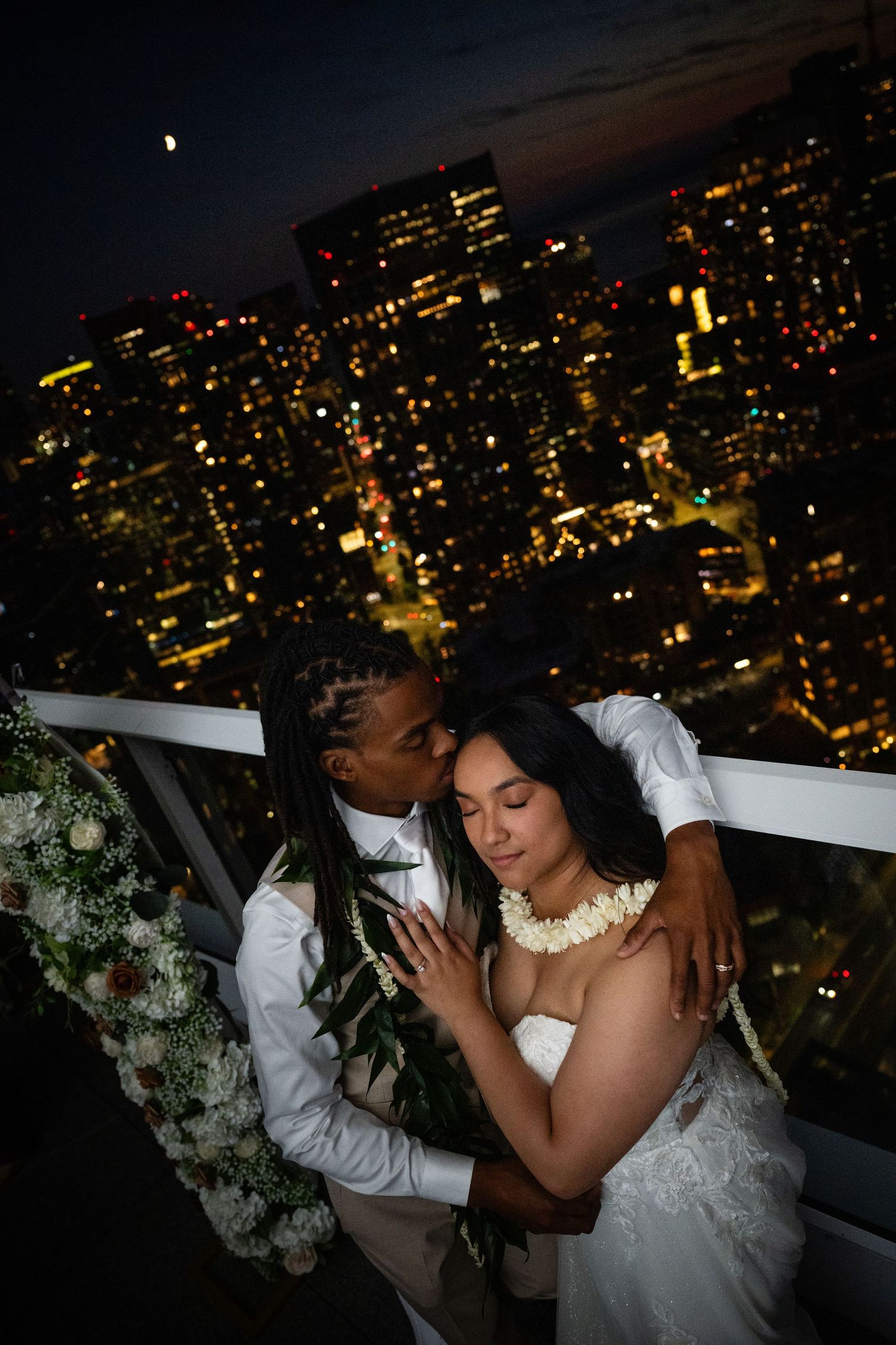 Couple dancing under city lights at night on a rooftop with illuminated skyscrapers in the background.