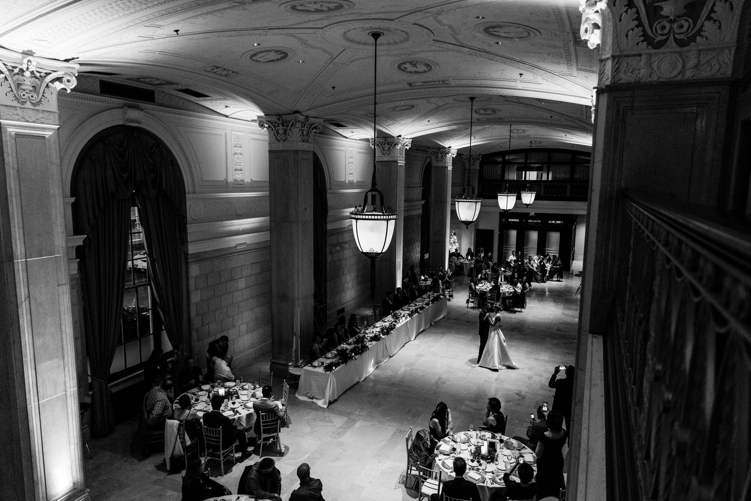 Black and white photograph of an elegant ballroom reception with hanging lanterns and classical architecture.