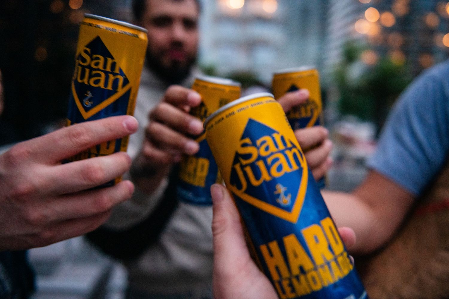 Friends clinking San Juan beer cans together during a rooftop celebration.