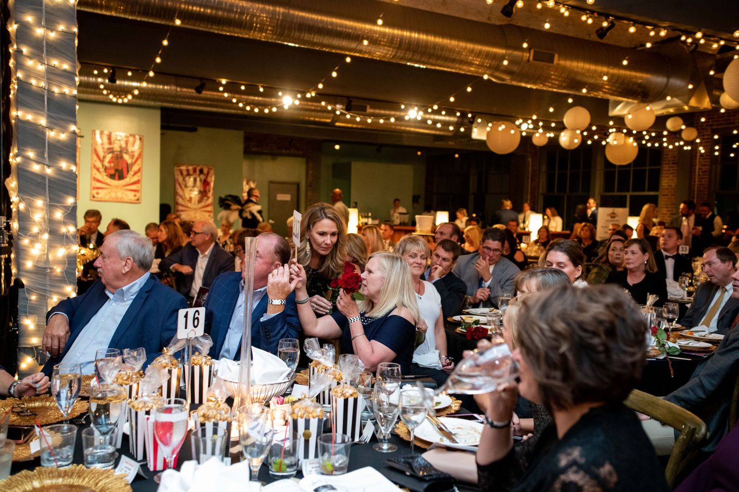 Elegant dinner event with guests seated at tables decorated with string lights and paper lanterns.