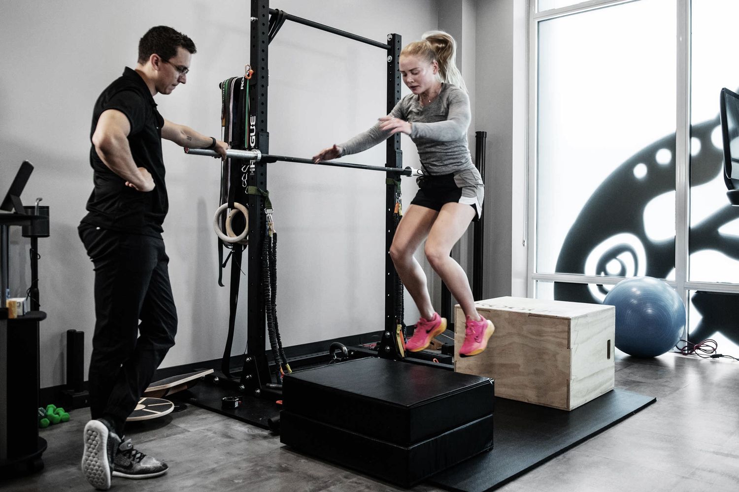 Trainer supervising client performing box jump exercise in gym.