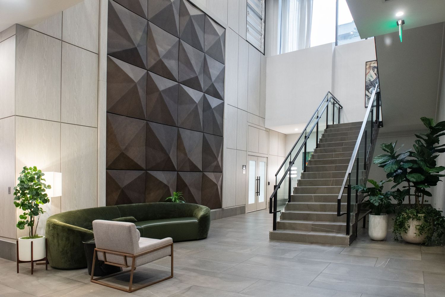 Modern lobby with geometric wall panels, curved staircase, and green accent seating.