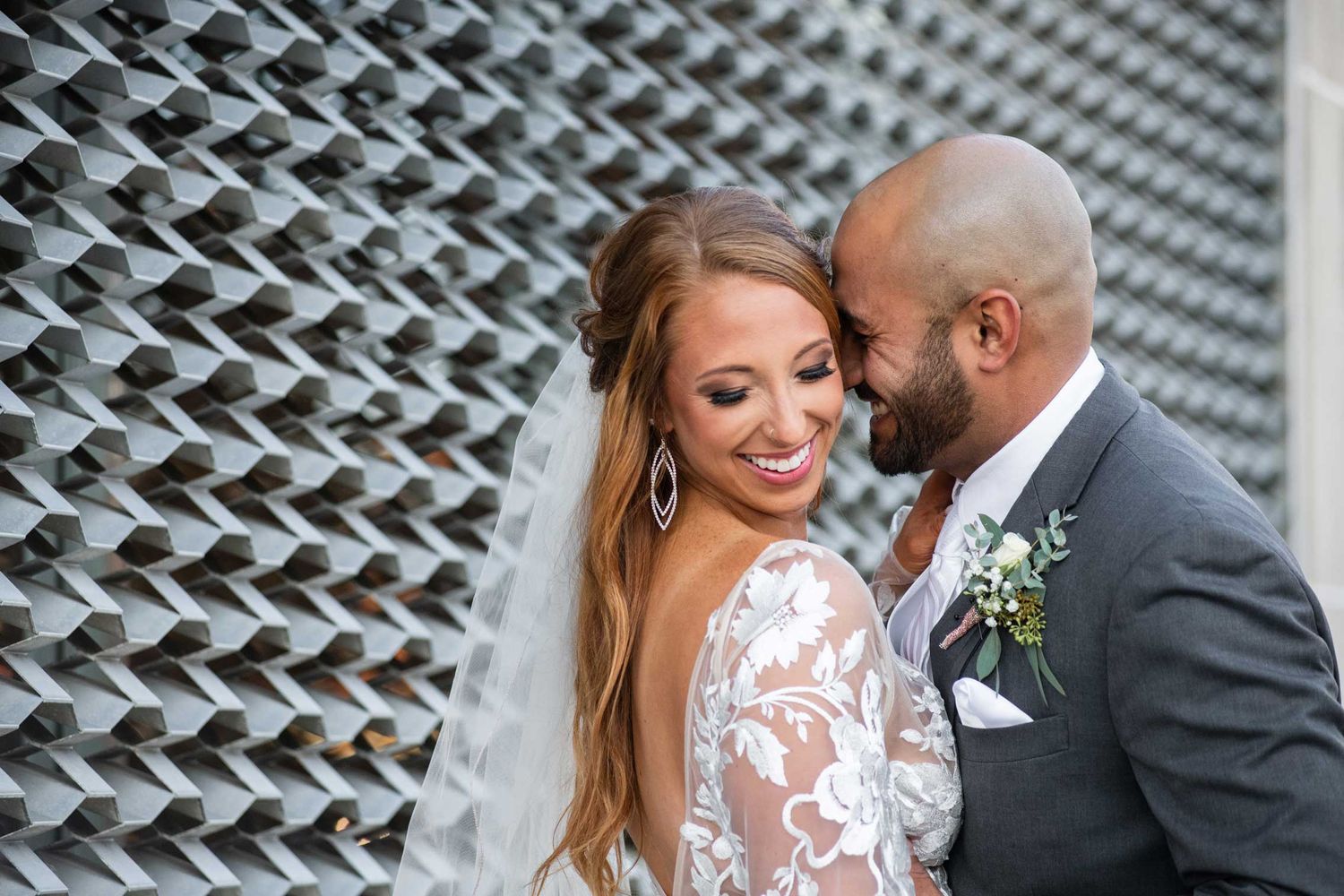Newlywed couple sharing intimate moment against geometric patterned wall.