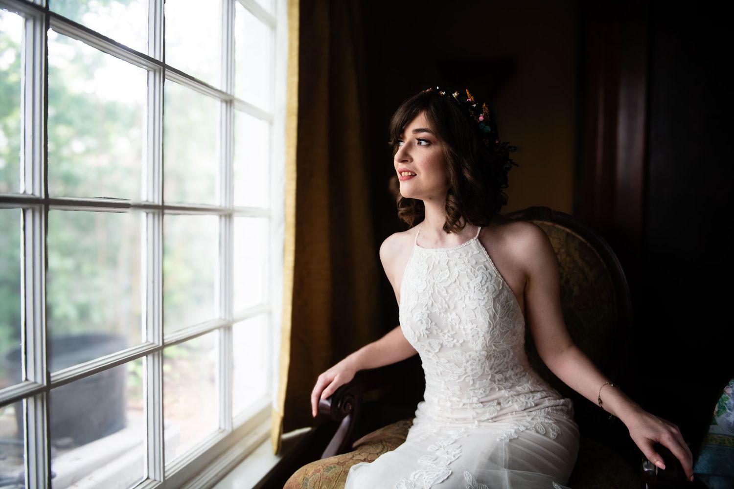 Elegant bridal portrait by a window showing detailed lace dress and crown.