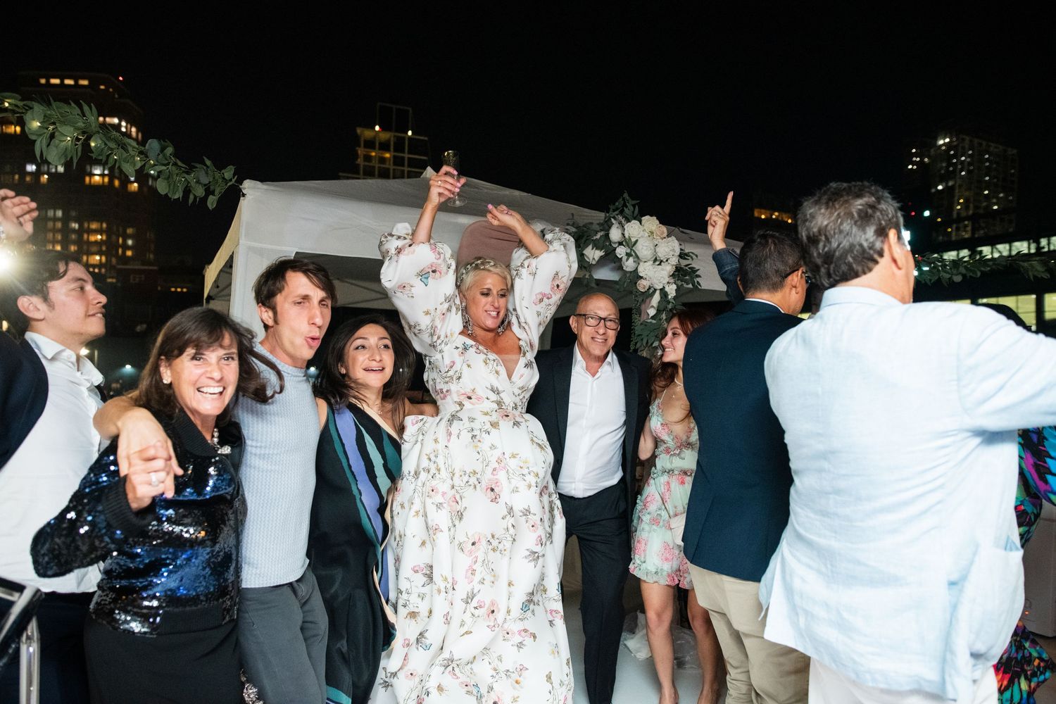 Wedding party celebrating with arms raised during an evening outdoor reception.