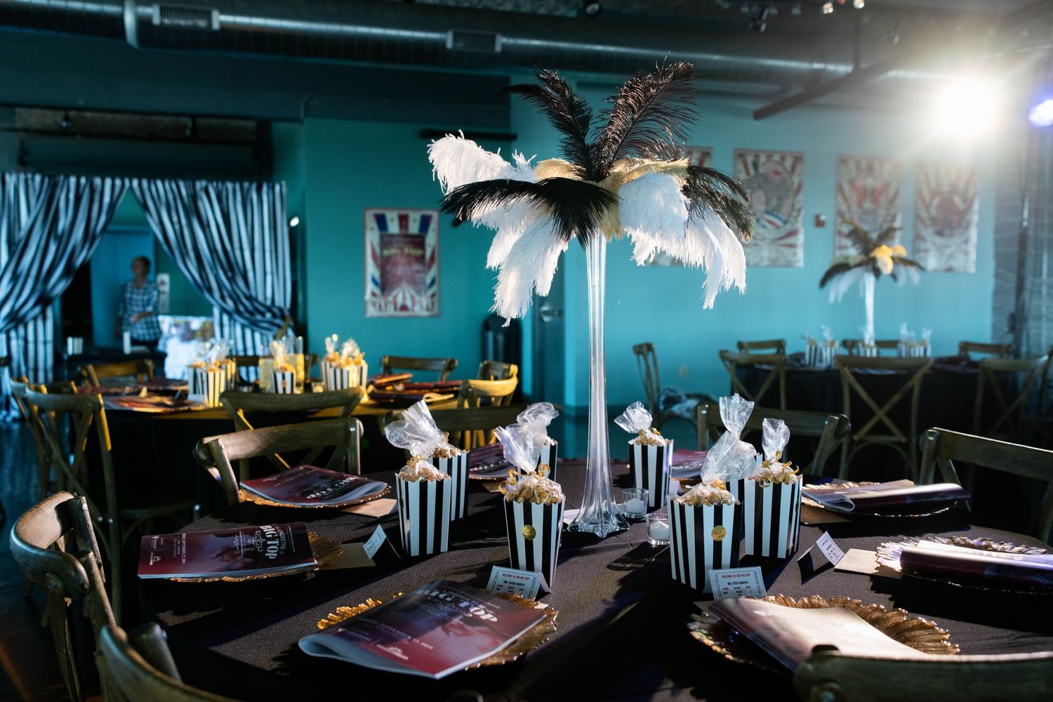 Elegant table settings with black and white striped accents and feather centerpieces in a teal-walled event space.