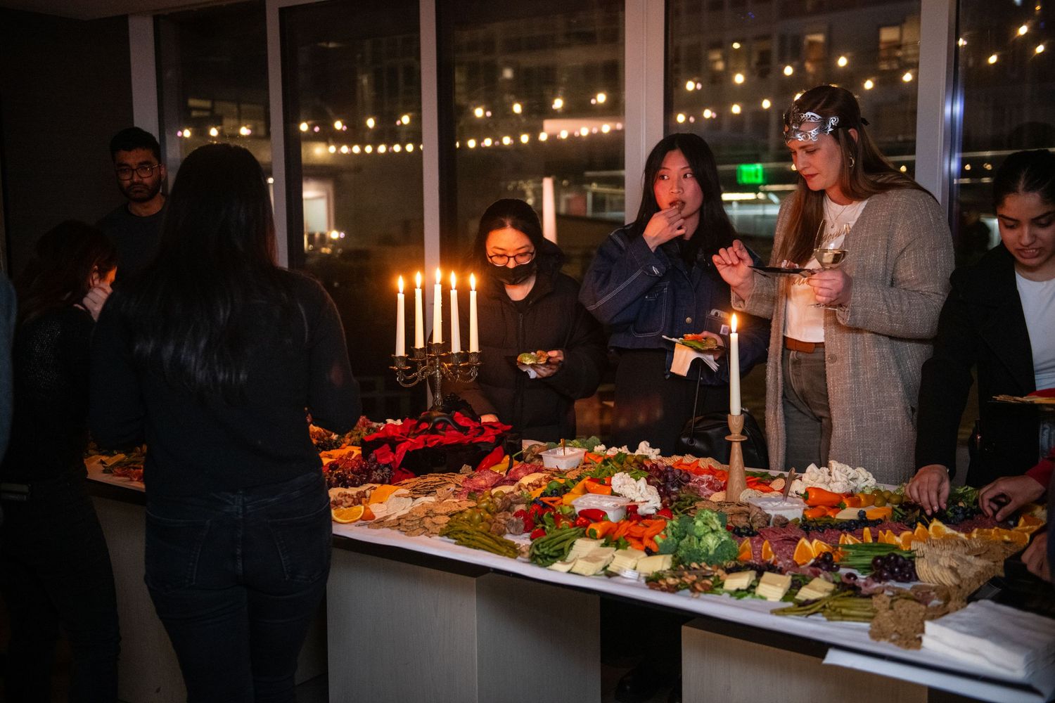 Buffet table with candles and appetizers as guests gather to enjoy food and drinks at an evening party.
