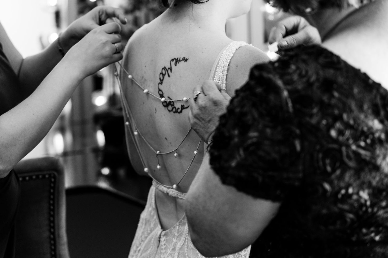 Close-up black and white shot of a delicate lace detail being adjusted on a wedding dress.