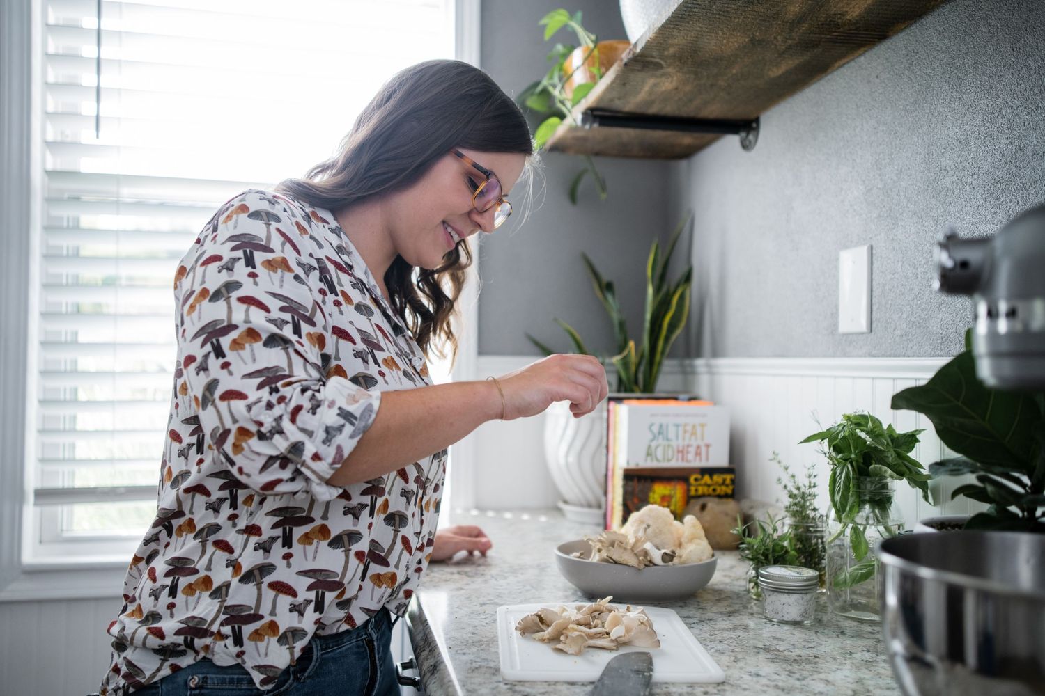 Cooking preparation scene in a bright kitchen with marble counters and wooden shelving.