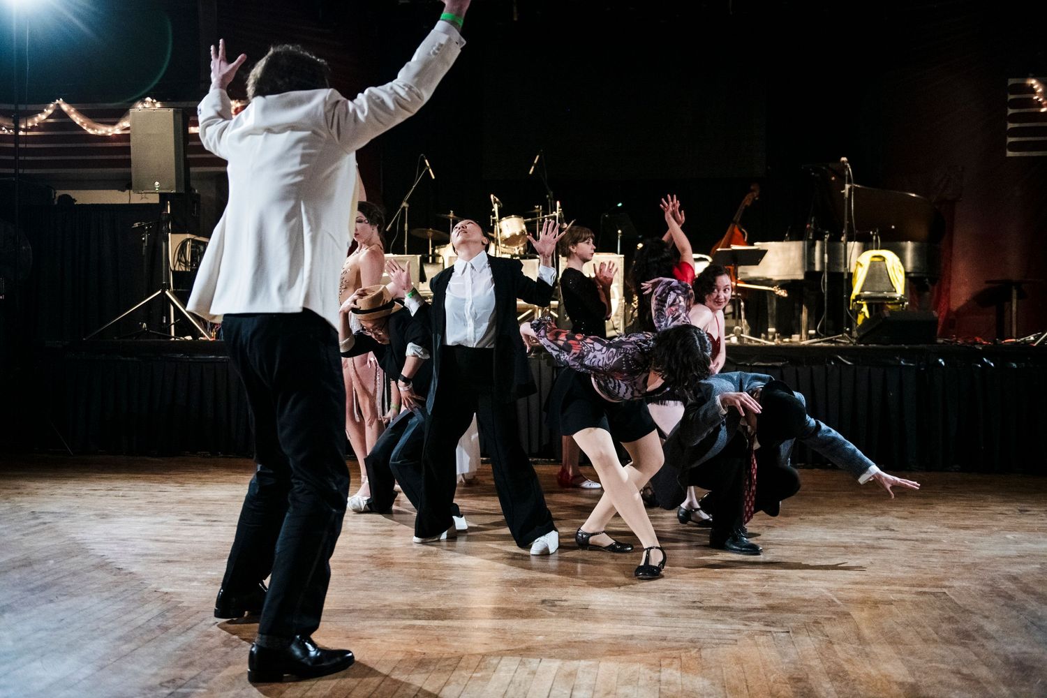 Dancers strike dramatic poses during a swing dance performance with live band setup.