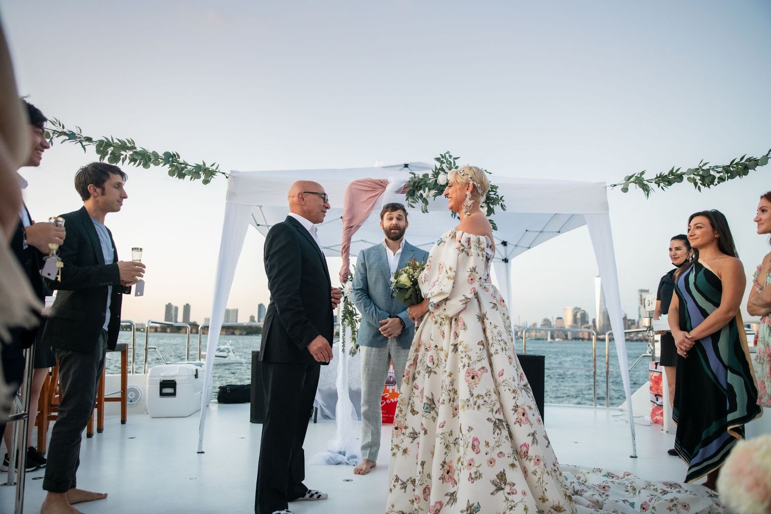 Waterfront wedding ceremony under white canopy with city skyline backdrop.