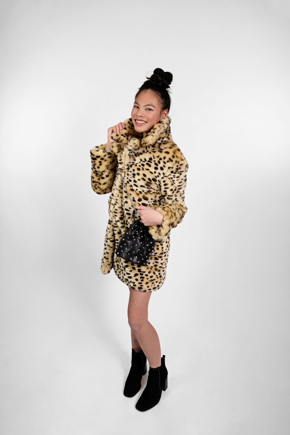 Model wearing leopard print faux fur coat and black ankle boots poses against white background.