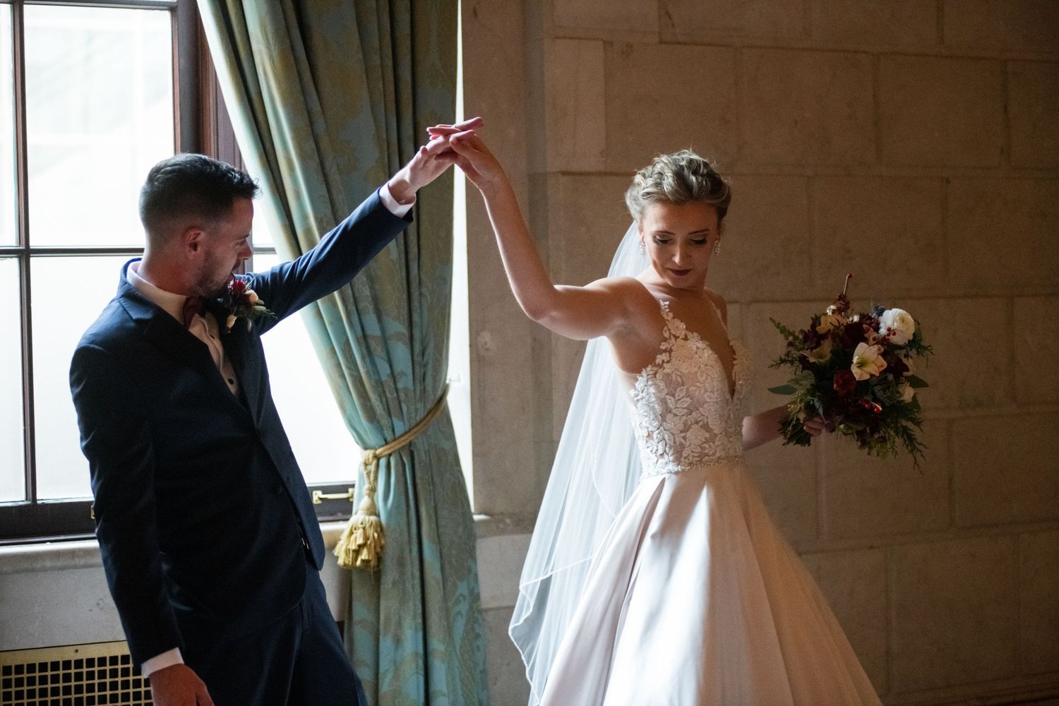 Couple celebrating with playful dance move in elegant venue with green curtains.