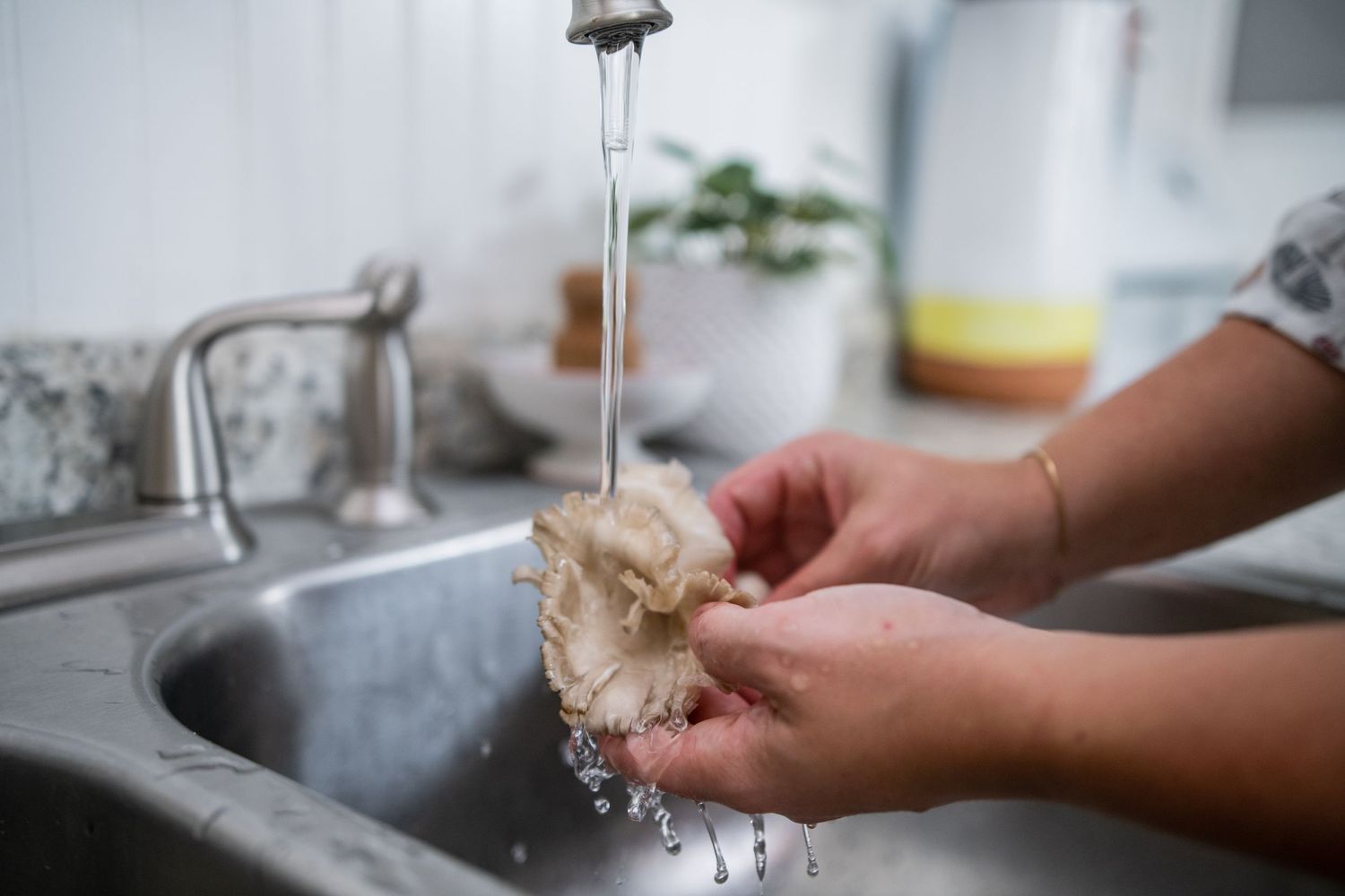 Close-up of hands washing under running water in a stainless steel sink.