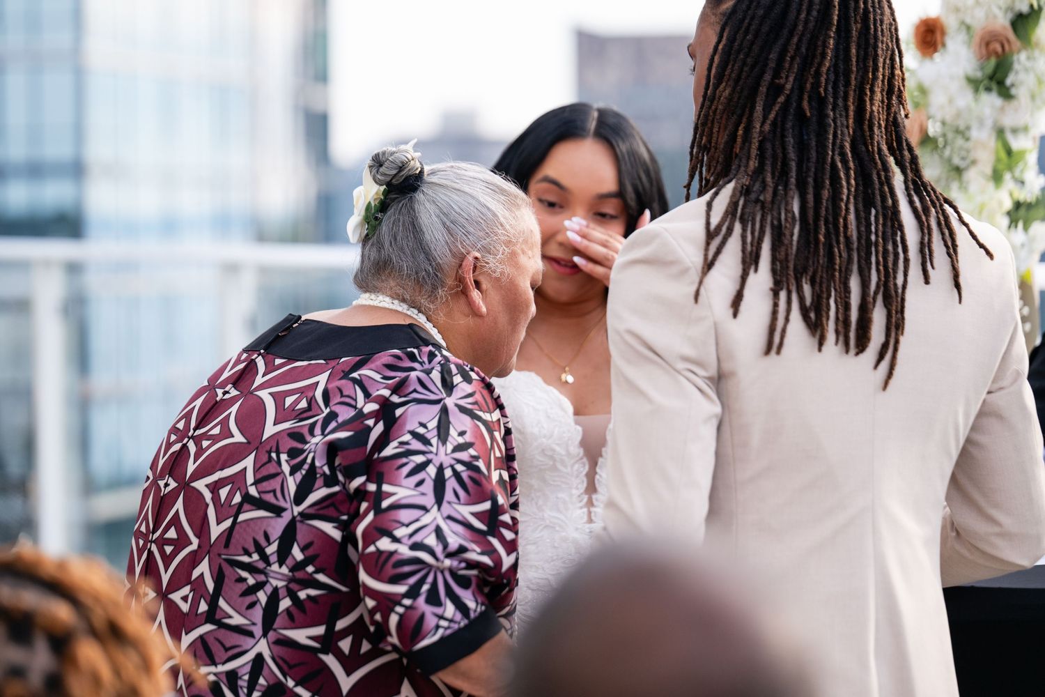 A group of people share a warm embrace in a sunlit setting with modern glass windows visible in the background.