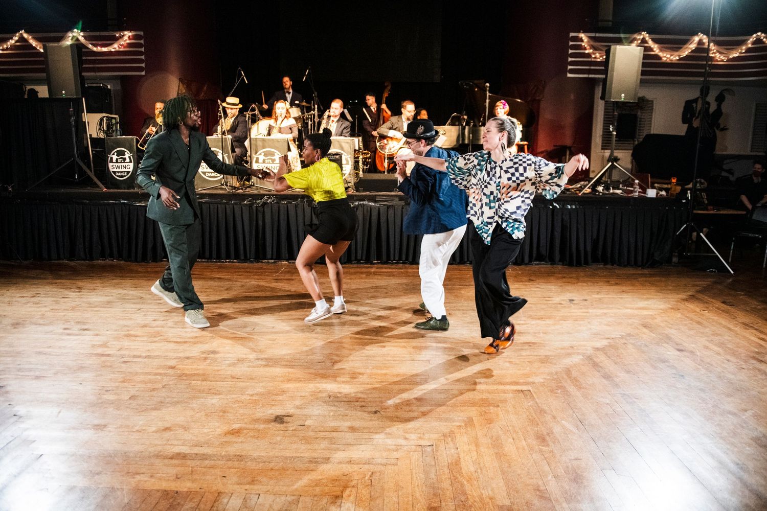 Dancers execute dynamic swing dance moves during performance with live band in background.