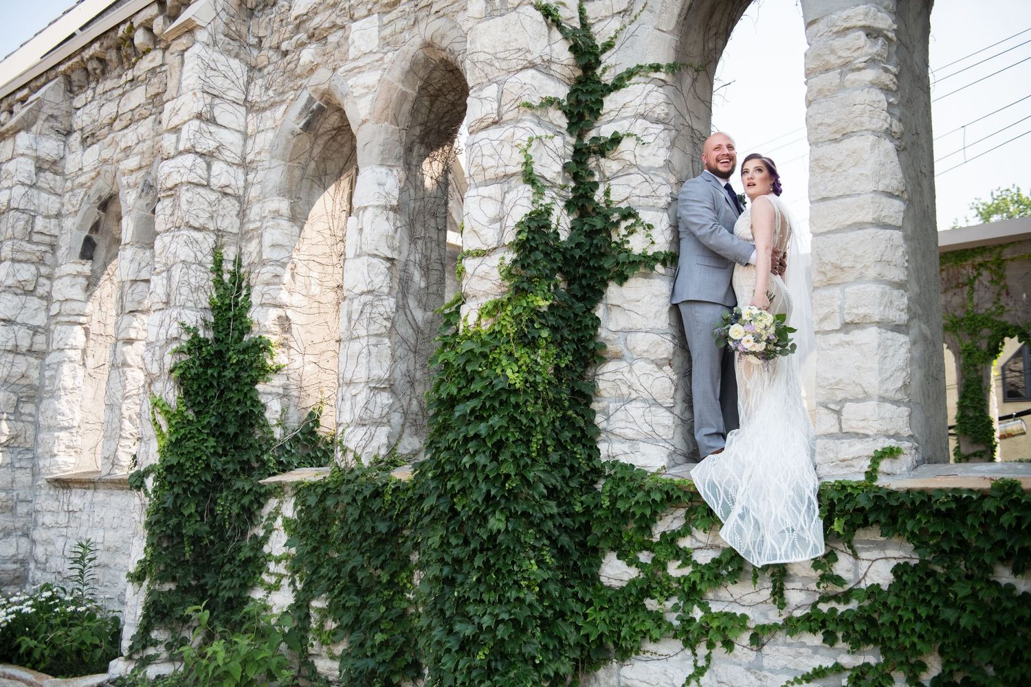 A couple stands on stone steps adorned with climbing ivy at their elegant outdoor wedding venue.