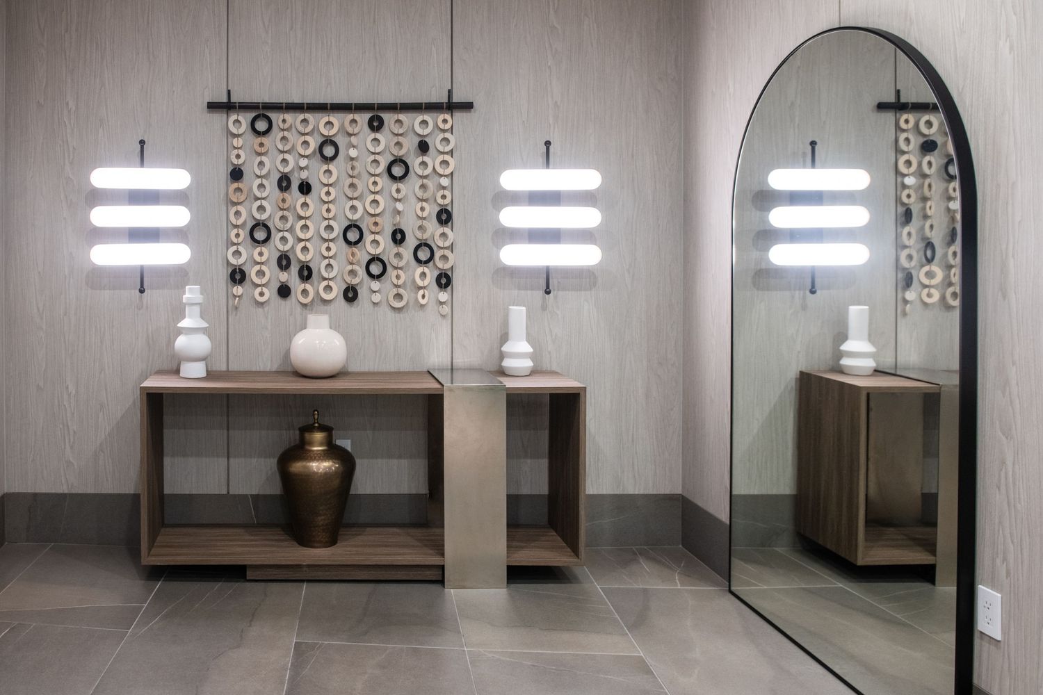 Modern hallway featuring illuminated art pieces, arched mirror, and decorative wall hanging.