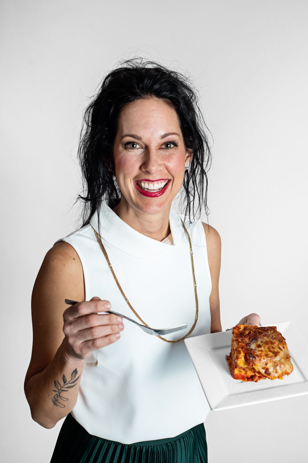 Person in purple top joyfully eating from plate against white background.