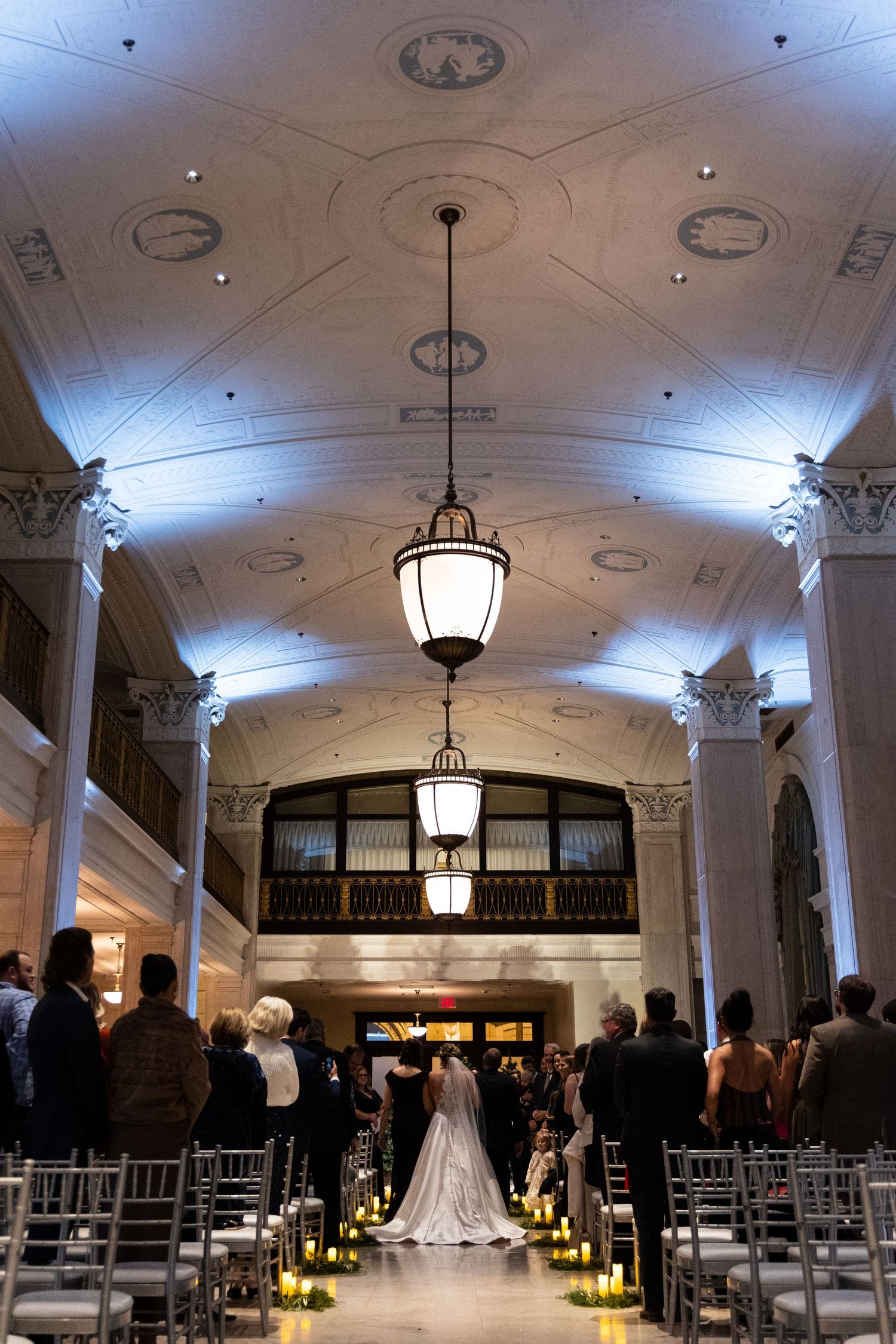 Wedding ceremony venue with ornate ceiling, hanging lanterns, and aisle lined with chairs.
