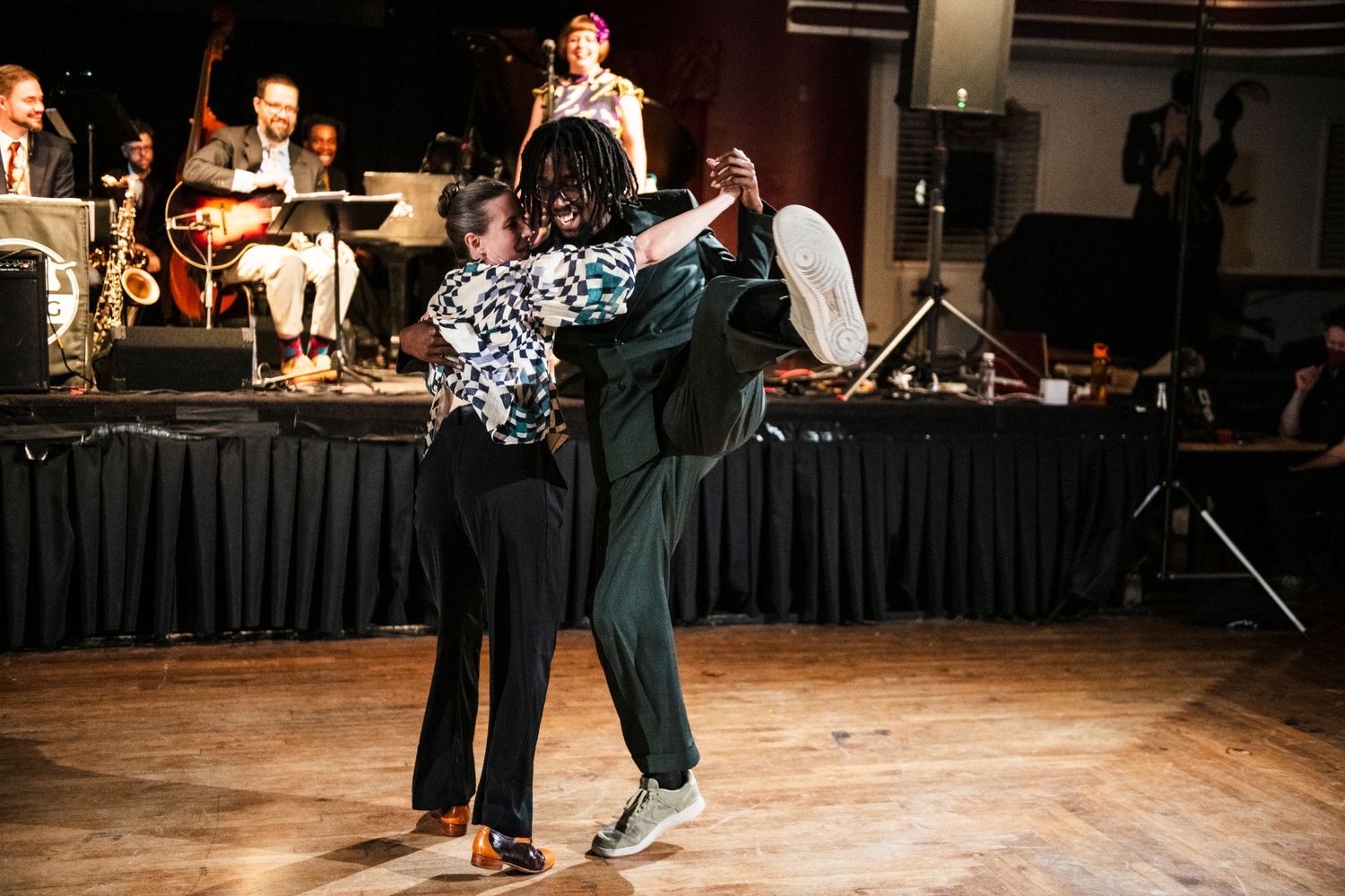 Swing dancers perform a graceful dance move in front of a live band on stage.