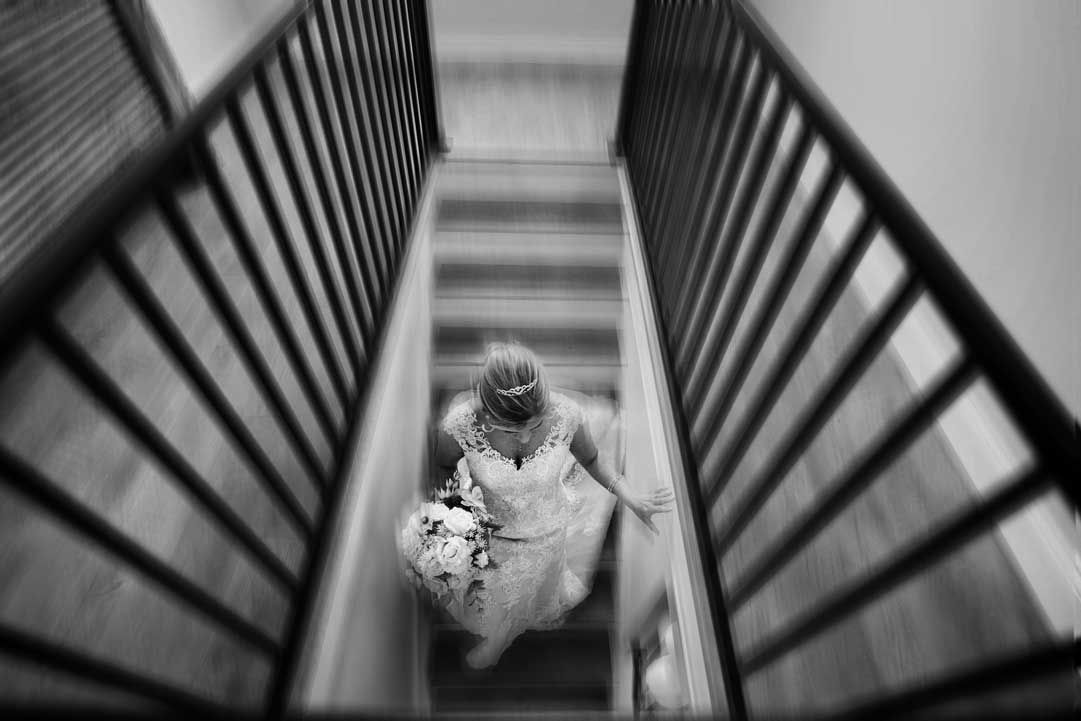 Black and white image of a person in formal attire descending stairs viewed through railings.