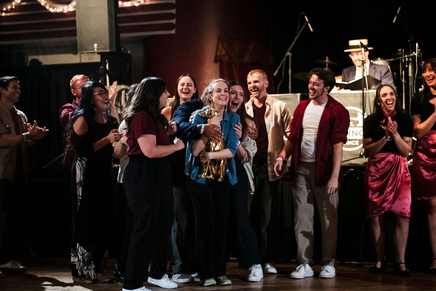 Performers celebrate together on stage during an indoor show with vintage lighting.