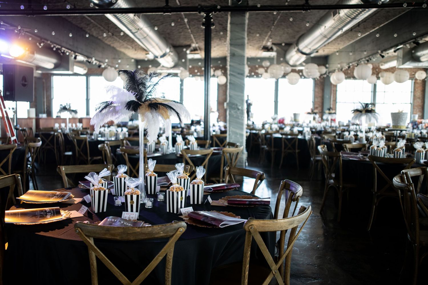 Large event venue with exposed ceiling, dramatic lighting, and tables set with black and white striped decor.