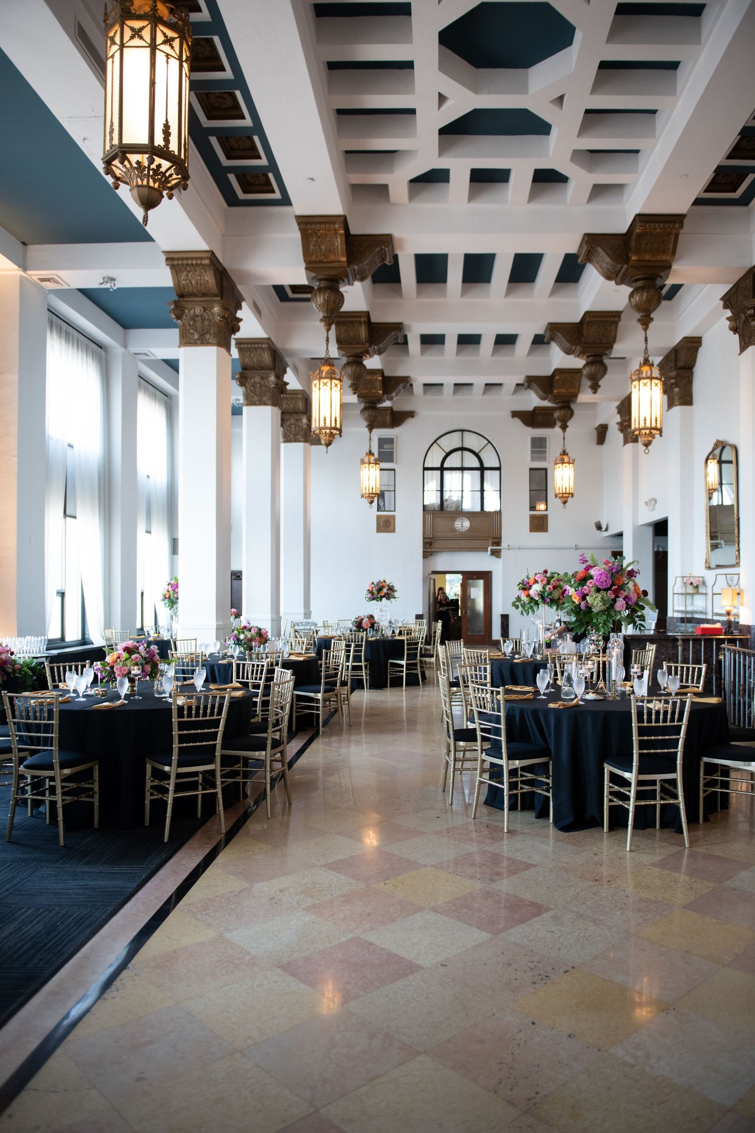 Elegant ballroom with ornate ceiling, hanging lanterns and round tables set for a formal event.