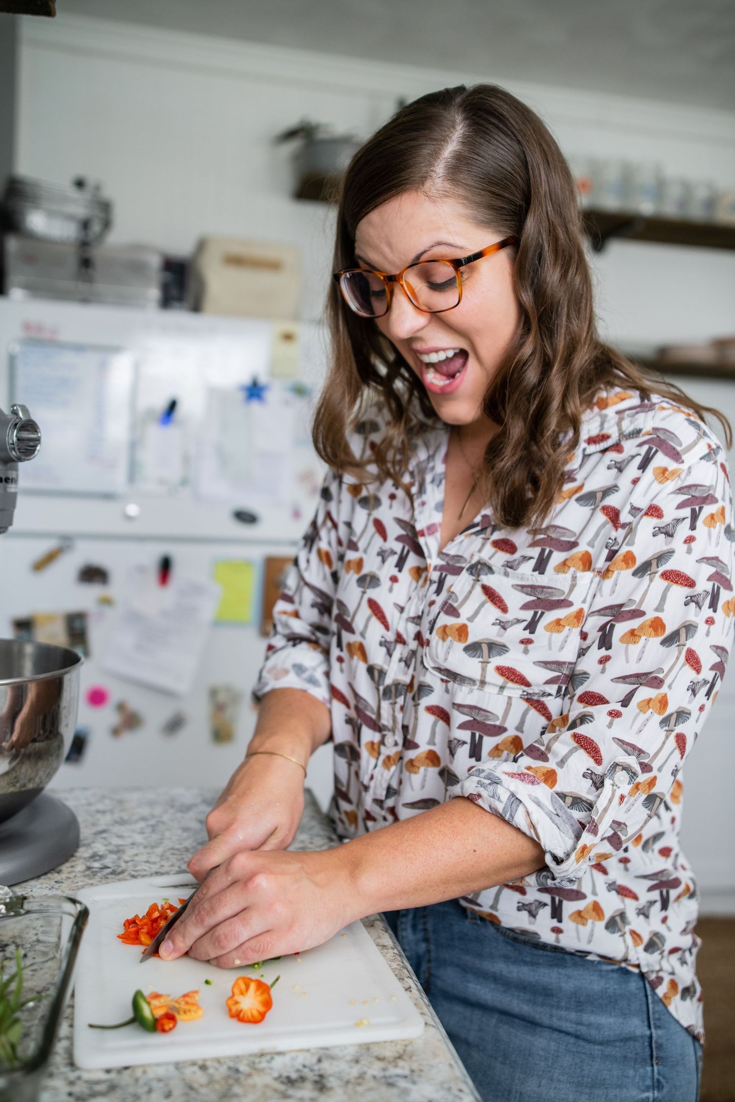 A cook in glasses and a patterned shirt chops ingredients in a bright kitchen with enthusiasm.