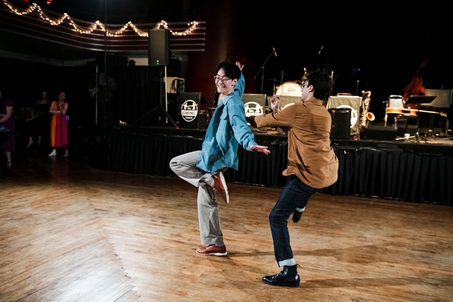 Dancers execute stylish kicks during a swing dance performance on a wooden floor.