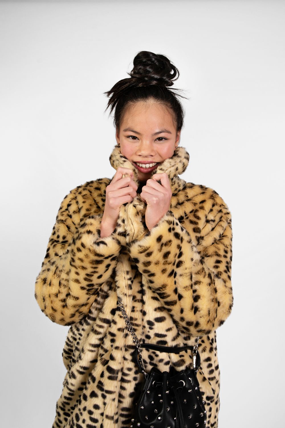 Person in leopard print coat snuggles into cozy collar against white backdrop.