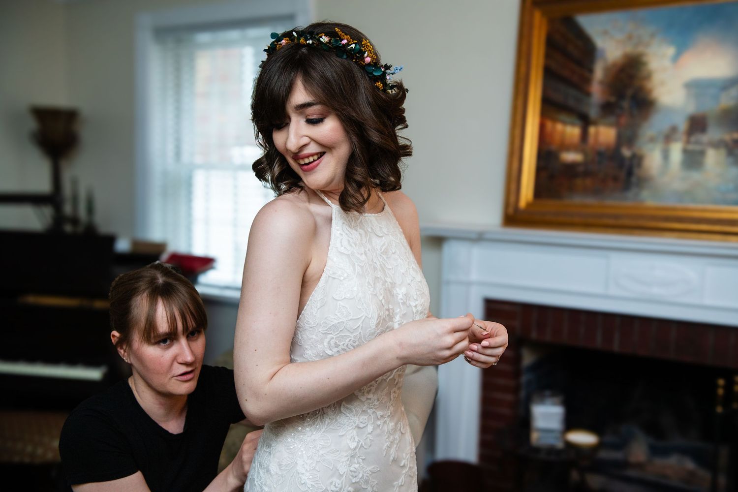 A person in a white lace wedding dress getting ready with assistance.