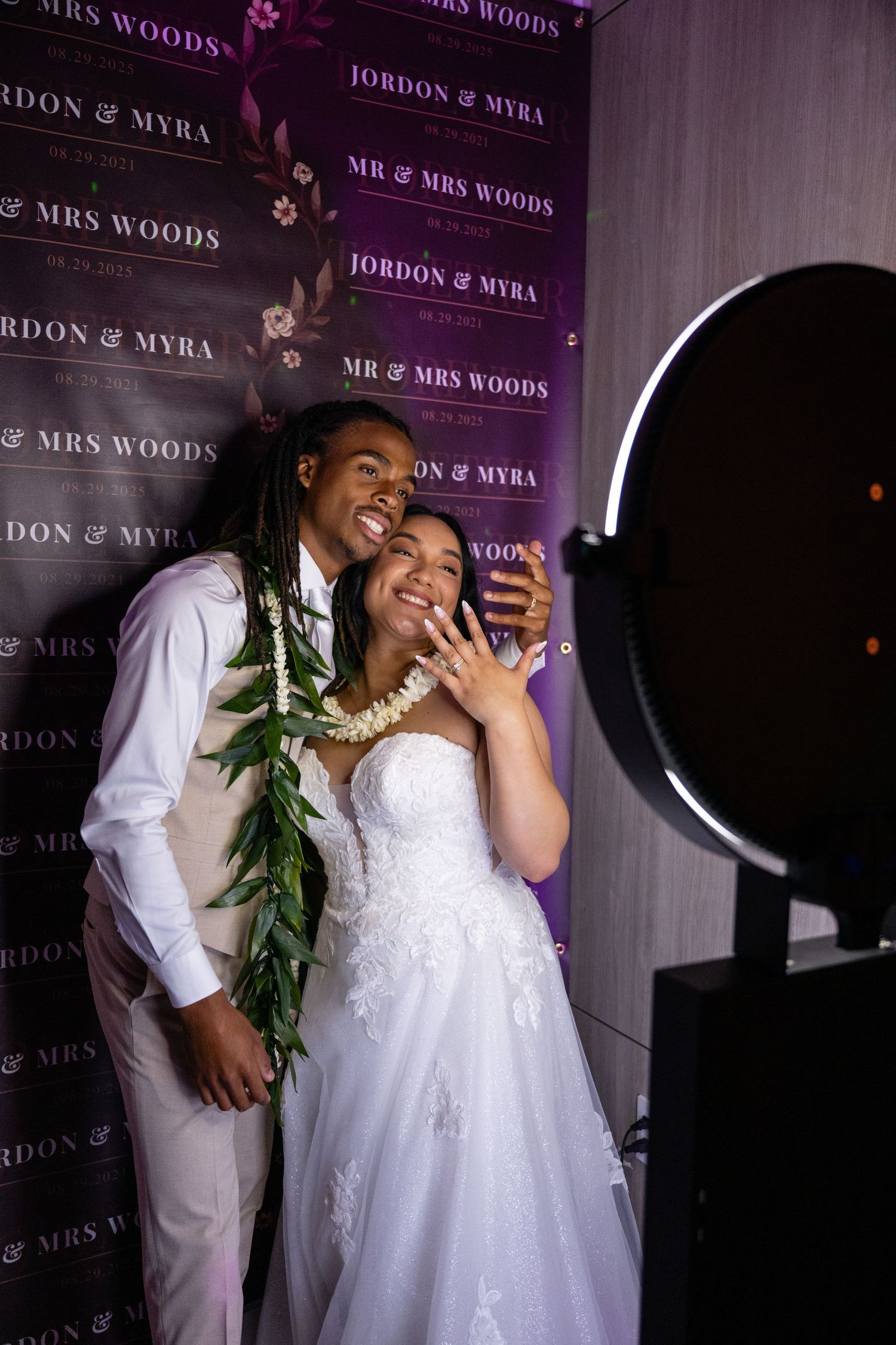 Wedding couple shares a joyous laugh against a purple backdrop with event signage.