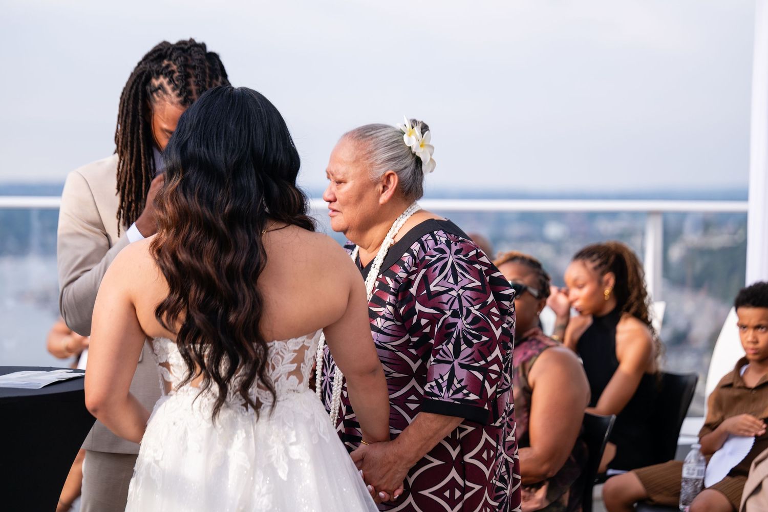 Wedding reception guests dancing outdoors with ocean views in the background during sunset.