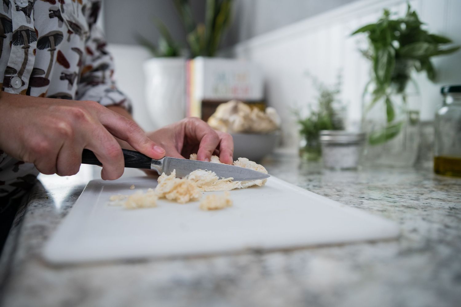Close-up of hands chopping ingredients on a white cutting board in a modern kitchen.