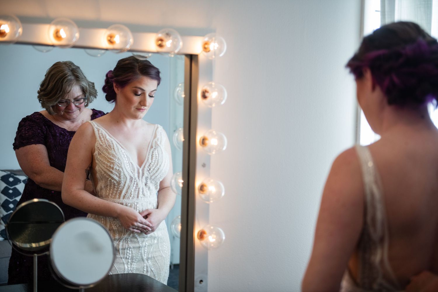 Wedding preparations in a dressing room with illuminated vanity mirror and bridal party getting ready.