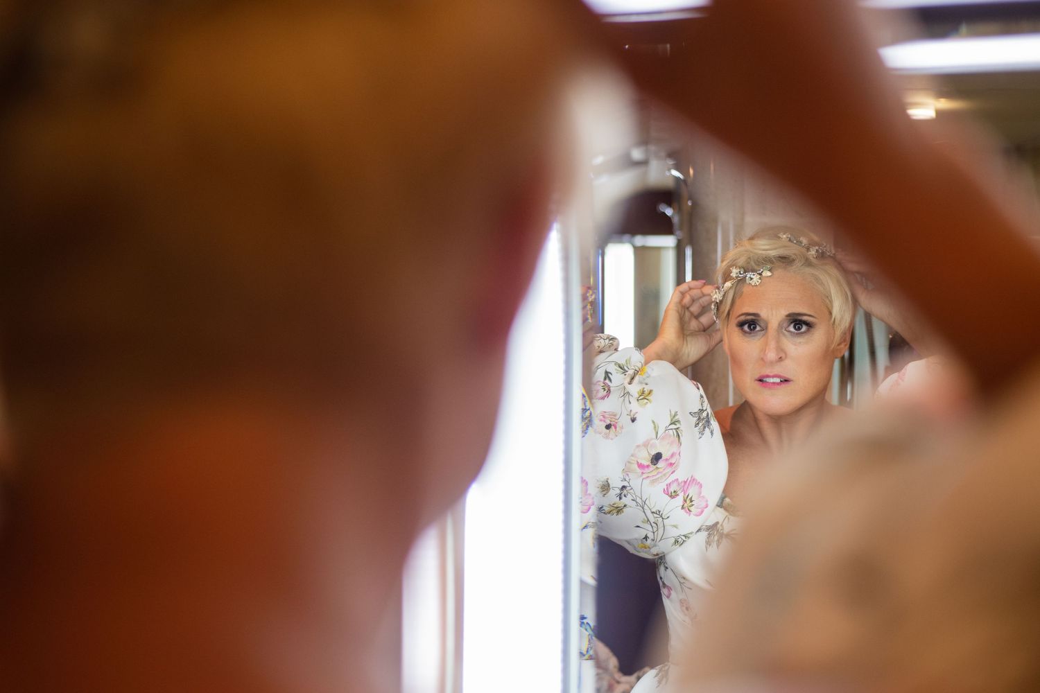 Mirror reflection showing bride getting ready in floral robe during wedding preparations.